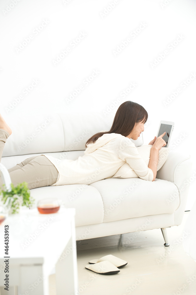 ソファに寝転んでタブレットPCを見る女性 ソファに寝転んでタブレットPCを見る女性
