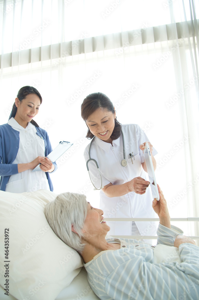 病院ベッドの老人を診察する女医と看護師 病院ベッドの老人を診察する女医と看護師