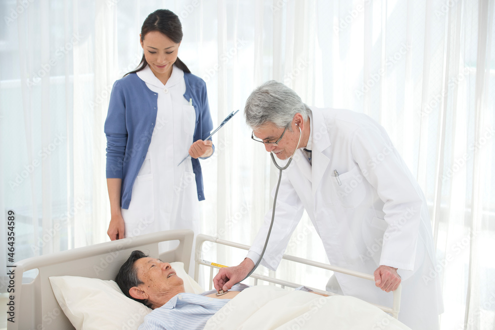 病院ベッドの老人を診察する医者と看護師 病院ベッドの老人を診察する医者と看護師