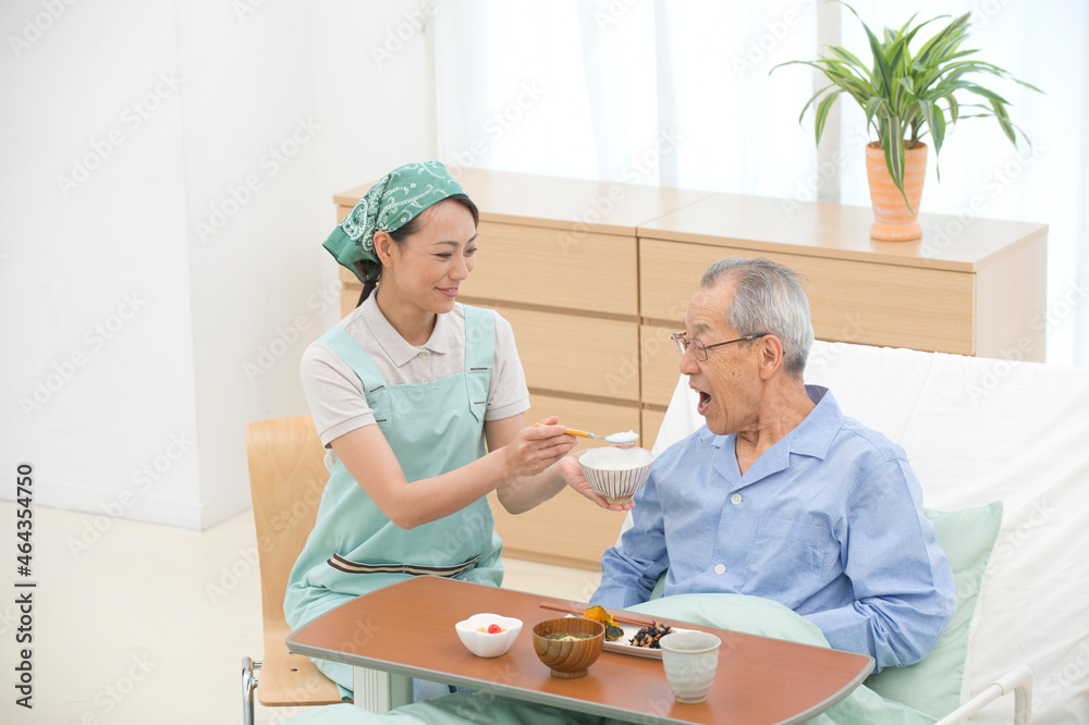 介護ベッドの老人に食事をさせる介護ヘルパー 介護ベッドの老人に食事をさせる介護ヘルパー