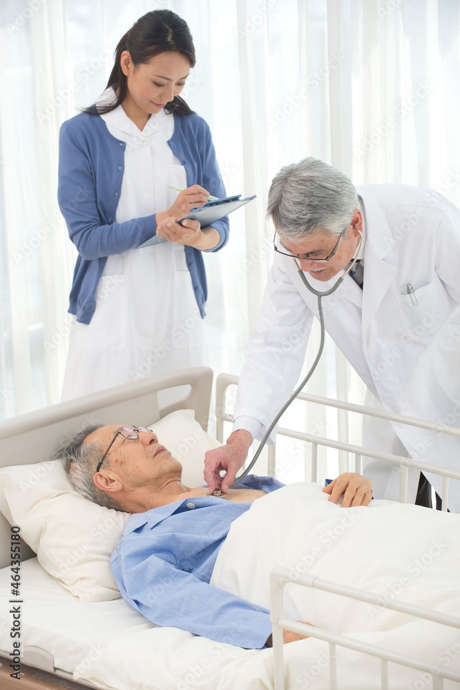 病院ベッドの老人を診察する医者と看護師 病院ベッドの老人を診察する医者と看護師