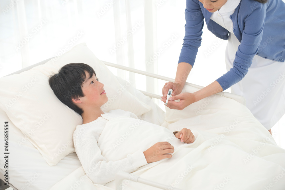 病院ベッドの男の子に体温計を渡す看護師 病院ベッドの男の子に体温計を渡す看護師