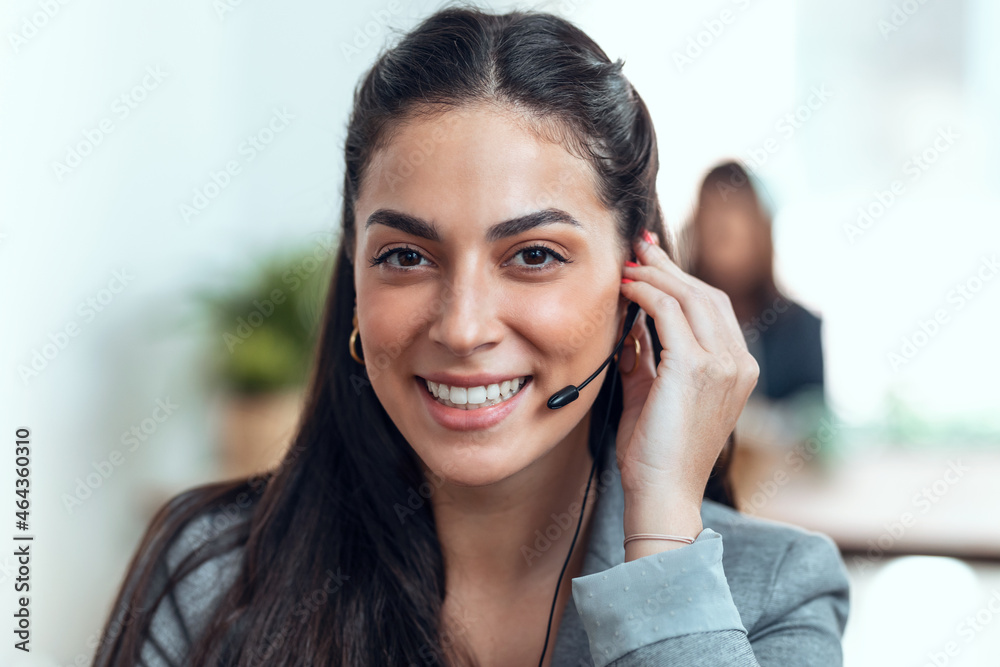 Smart business woman talking with earphones while doing a video call looking at camera in the office. Smart business woman talking with earphones while doing a video call looking at camera in the office.