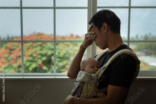 A tired stressed out father holding his sleeping baby at home. Postpartum depression.