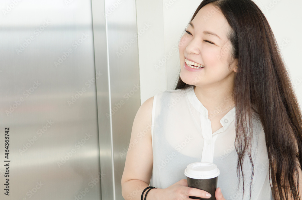 エレベーター前でコーヒーカップを持って笑うOL