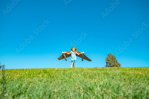 Kid pilot with toy jetpack against green grass and sky background. Happy child playing outdoors. Happy childhood.