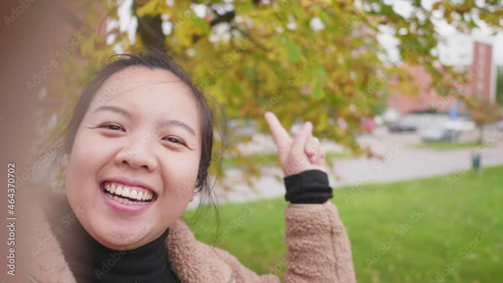 Close up of Happy Asian woman taking video call on smartphone at the park in Autumn, woman wearing light brown coat, yellow leaf on the tree, Beautiful day in Autumn season, River background in Sweden Close up of Happy Asian woman taking video call on smartphone at the park in Autumn, woman wearing light brown coat, yellow leaf on the tree, Beautiful day in Autumn season, River background in Sweden