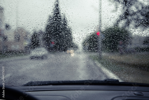The road and rain on the glass of the car, the traffic light is visible.