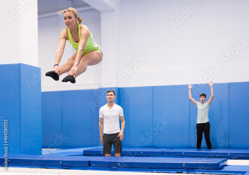 Focused female gymnast jumping on professional trampoline, exercising L shape in jump during training © JackF