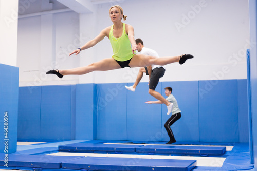 Young athletic woman practicing side split in jump on trampoline in sports center..