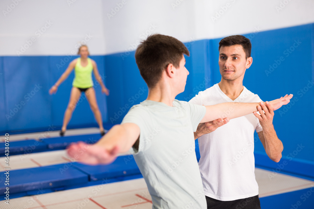 Male instructor helping teenage boy warming up before trampoline training in fitness center