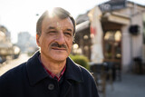Front view portrait of senior caucasian man with mustaches standing in the city in winter or autumn day looking to the side wearing coat close up copy space