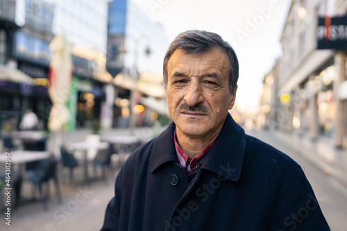 Front view portrait of senior caucasian man with mustaches standing in the city in winter or autumn day looking to the camera wearing coat close up copy space