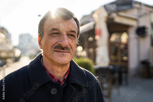 Front view portrait of senior caucasian man with mustaches standing in the city in winter or autumn day looking to the side wearing coat close up copy space