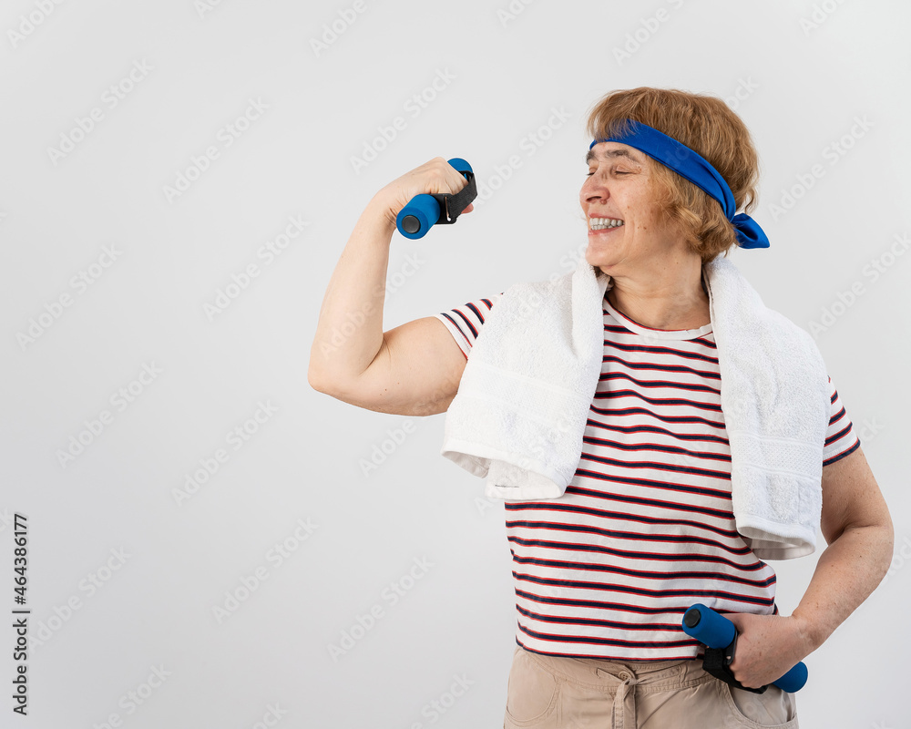 An elderly woman with a blue bandage on her head trains with dumbbells on a white background An elderly woman with a blue bandage on her head trains with dumbbells on a white background