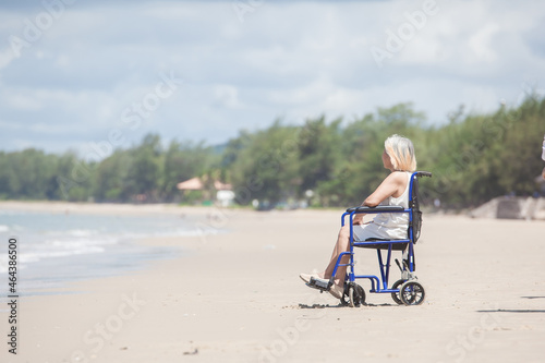 woman asia sitting in a wheelchair on the beach. Disabled handicapped woman is sitting on wheelchair at sunset on the beach