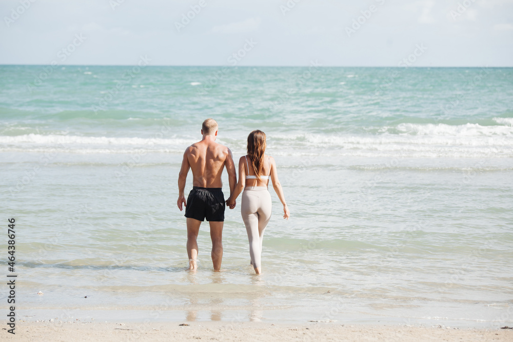 young couple walking at each other at beach. Romantic couple walking on sea, enjoying life and each other at honeymoon vacation. young couple walking at each other at beach. Romantic couple walking on sea, enjoying life and each other at honeymoon vacation.