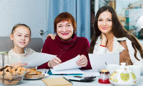 Smiling senior woman with daughter and granddaughter writing papers at home