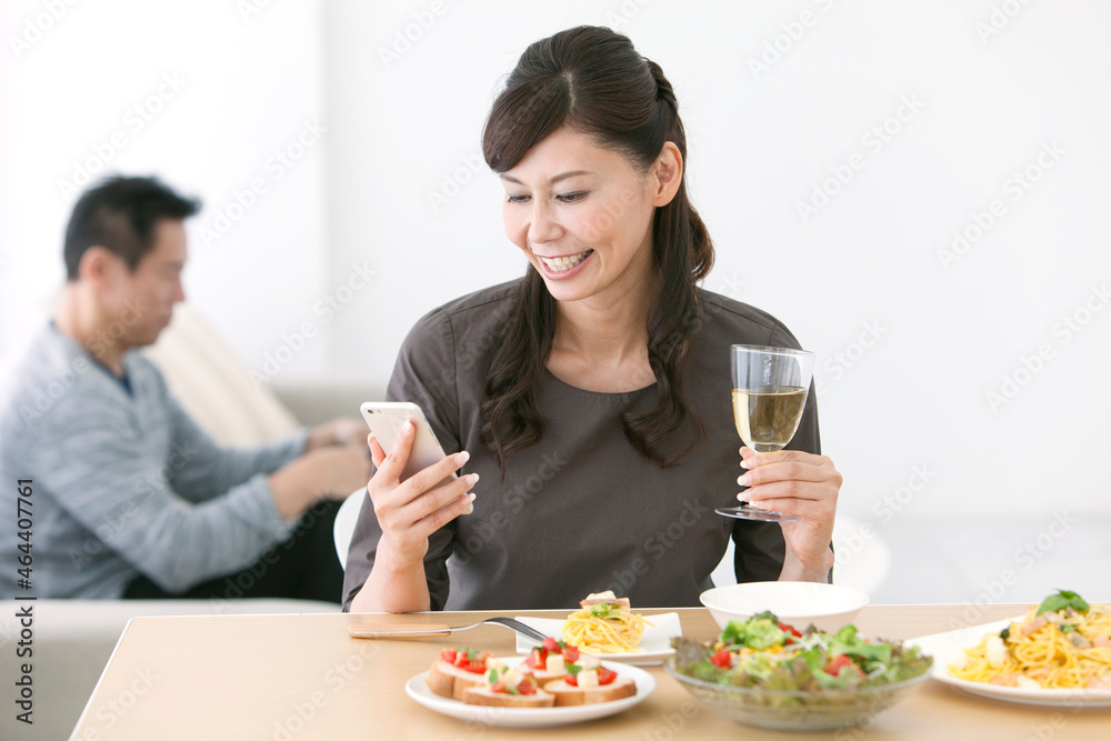 食卓でスマートフォンを操作する妻と夫 食卓でスマートフォンを操作する妻と夫