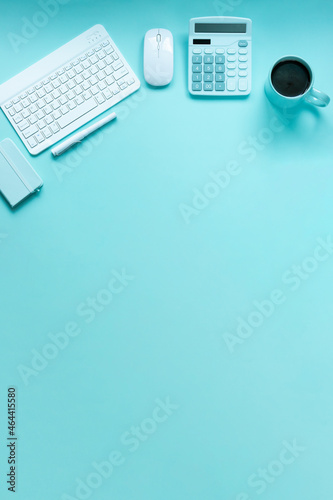 Top view of soft pastel blue theme desktop workspace which consists of calculator, notebook, pens, mouse, keyboard, and a cup of black coffee. With copyspace.
