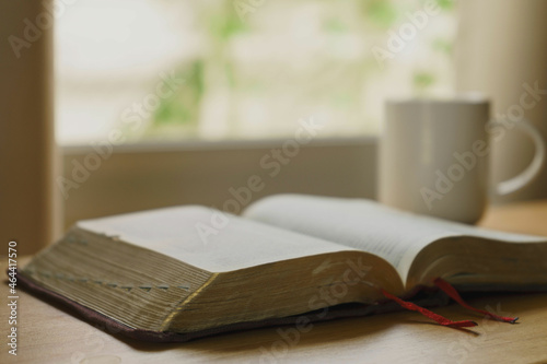 Fotografia Close up of open bible with a cup of coffee for morning devotion on wooden table with window light