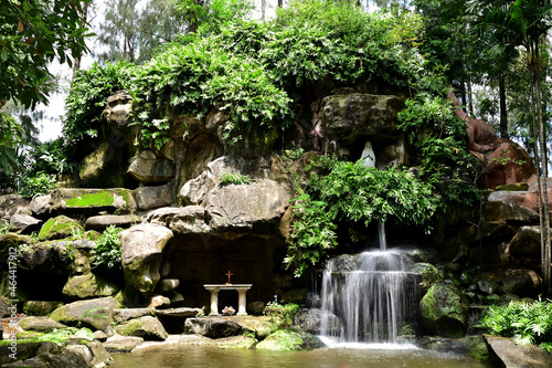 Statue of Our lady of grace virgin Mary view with natural background in Waterfall flows down from the rock cave at Thailand.