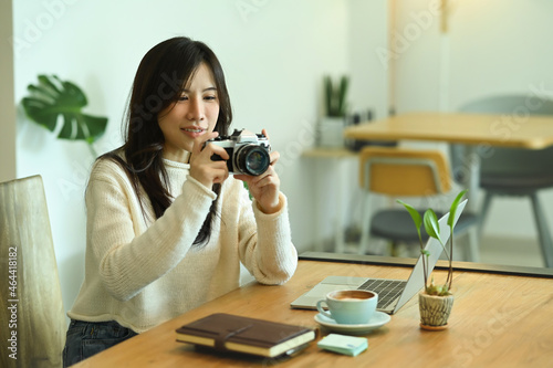 Smiling young woman holding camera and checking picture previews.