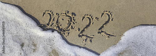2022 written in the sand of a beach on the edge of the foam of wave in panora...