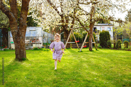 Happy little toddler girl having fun with playing in domestic garden. Smiling positive healthy child run and jump on backyard . Preschool girl laughing and crying. Active leisure and activity outdoors