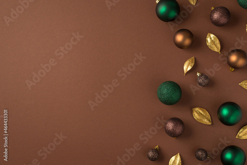 Top view photo of christmas tree decorations green brown golden balls and golden leaves on isolated brown background with empty space