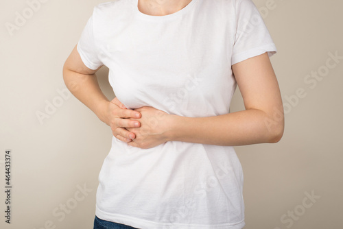 Cropped closeup photo of young woman in white t-shirt holding right upper abdomen with her hands on isolated grey background