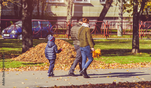 A married couple walks with their son in the autumn park