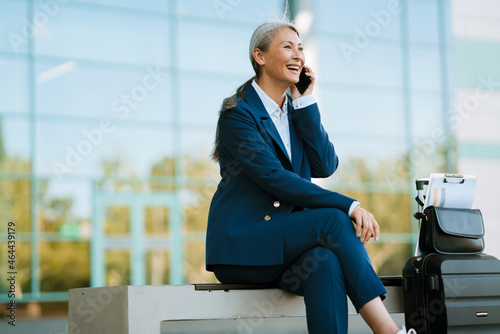 Grey asian woman talking on mobile phone while sitting at airport parking