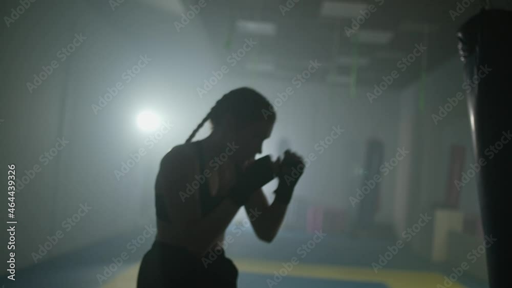 Female fighter trains his punches and defense in the boxing gym, contour lighting, female strikes fast. Female fighter trains his punches and defense in the boxing gym, contour lighting, female strikes fast.