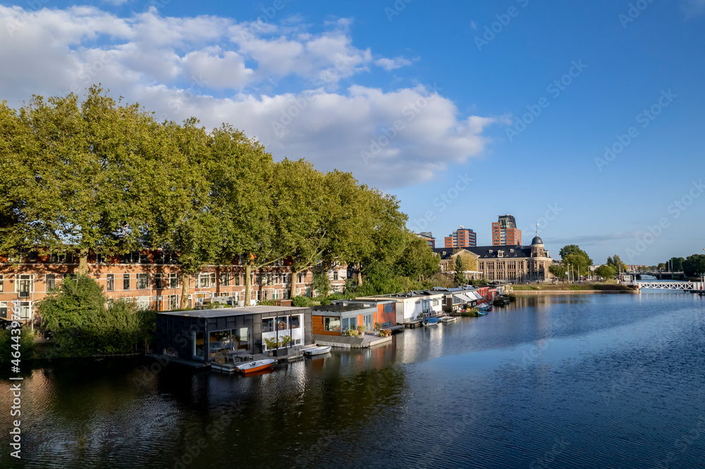 Naklejka premium Floating home boats on canal in city of Utrecht with Muntgebouw in the background against a blue sky with clouds and autumn colored trees
