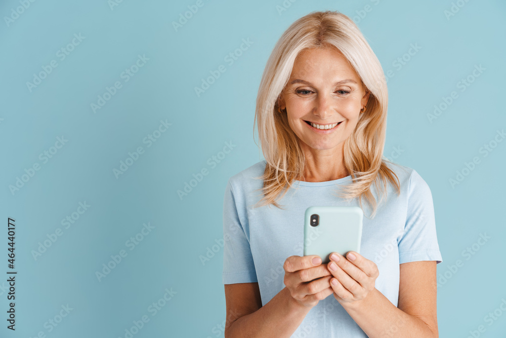 Mature blonde woman wearing t-shirt smiling and using cellphone Mature blonde woman wearing t-shirt smiling and using cellphone