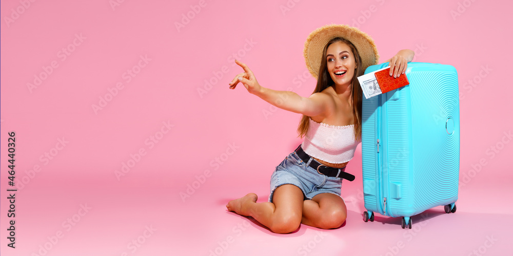 Glad girl with suitcase, tickets, money and passport are going to travel while pointing finger Glad girl with suitcase, tickets, money and passport are going to travel while pointing finger