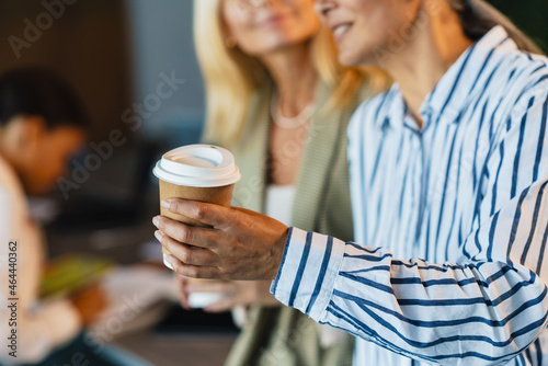 Adult multiracial women smiling and drinking coffee in office