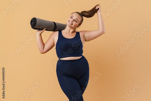 Young woman wearing sport suit smiling while posing with fitness mat