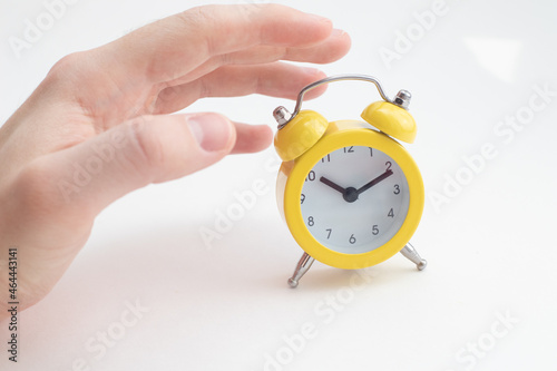 A hand slaps the yellow alarm clock to turn it off