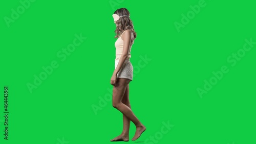 Side view of young sleepwalker woman in pajama with sleep mask on eyes sleep walking. Full body isolated on green screen background photo