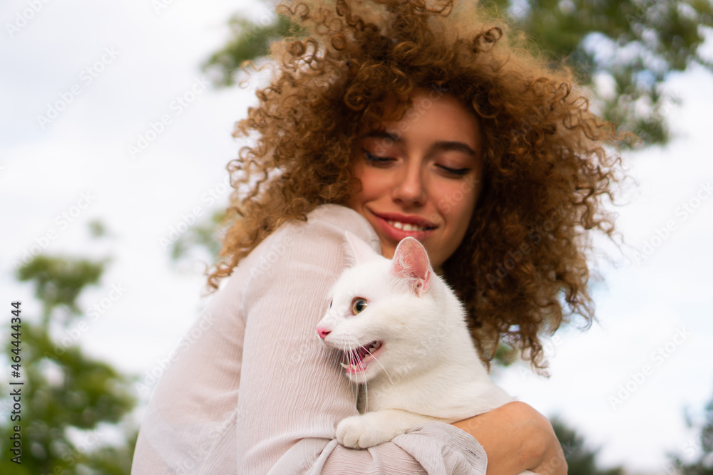 A beautiful teenage girl with curly hair holds a white cat close to her face. She is enjoying time with her pet. A beautiful teenage girl with curly hair holds a white cat close to her face. She is enjoying time with her pet.