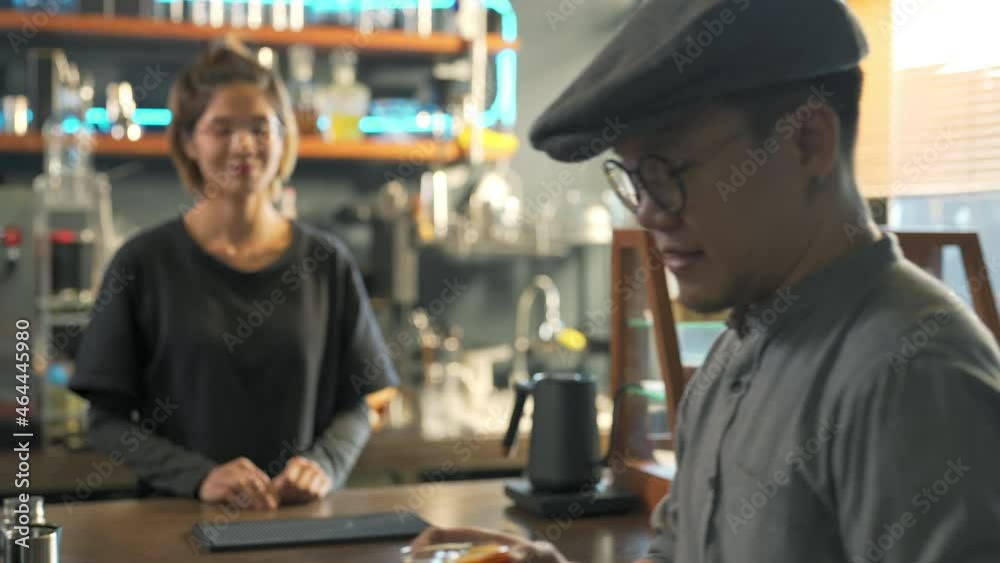Asian woman barista making iced black coffee with fresh orange juice in the glass. Female coffee shop waitress serving coffee to customer on counter at cafe. Small business restaurant owner concept.