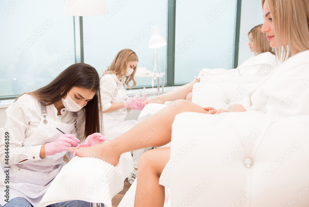 Obraz premium Foot treatment for two friends or sisters in SPA salon. Nail artist in beauty salon making pedicure for clients feet.