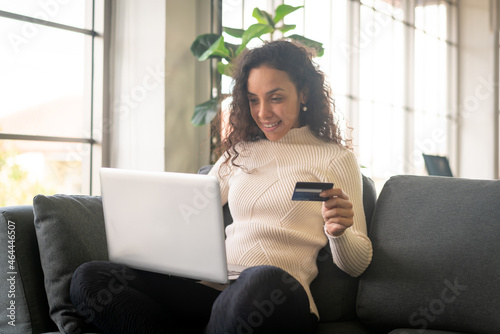 Latin woman using laptop and hand holding credit card for shopping on sofa