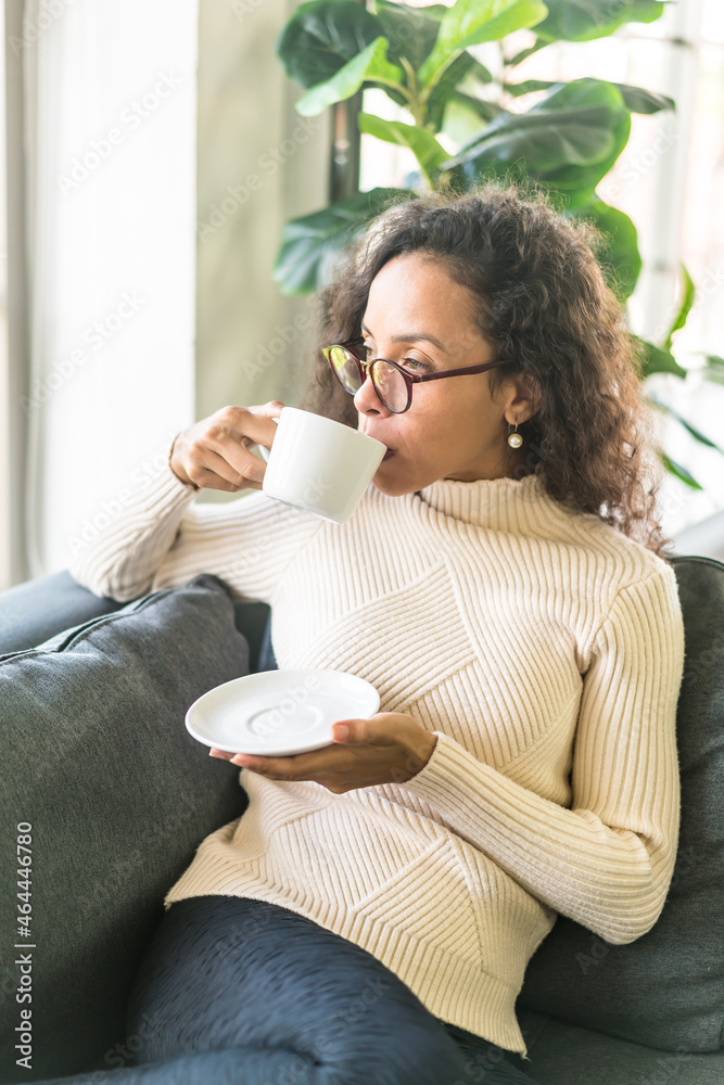 Latin woman drinking coffee on sofa at home Latin woman drinking coffee on sofa at home