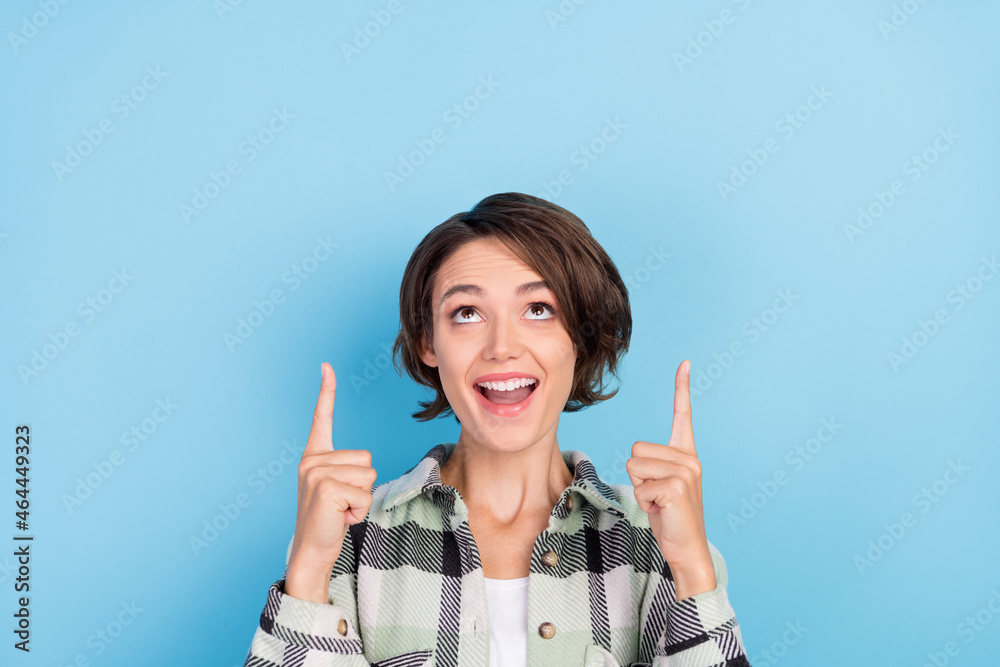 Photo of cute impressed young lady wear plaid shirt pointing fingers up looking empty space isolated blue color background Photo of cute impressed young lady wear plaid shirt pointing fingers up looking empty space isolated blue color background