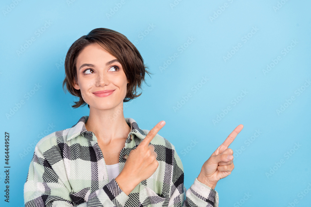 Photo of funny young brunette lady point look empty space wear plaid shirt isolated on blue color background Photo of funny young brunette lady point look empty space wear plaid shirt isolated on blue color background