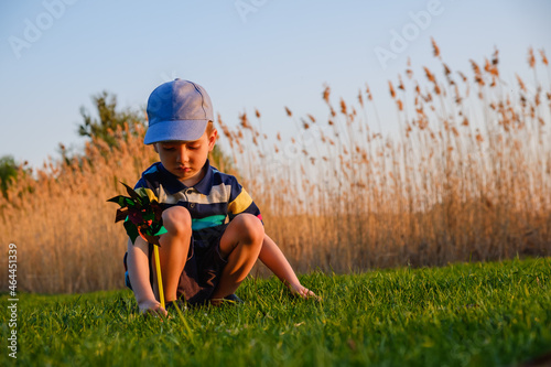 Boy playing with windmill in green grass of the beach on summer vacation concept for freedom