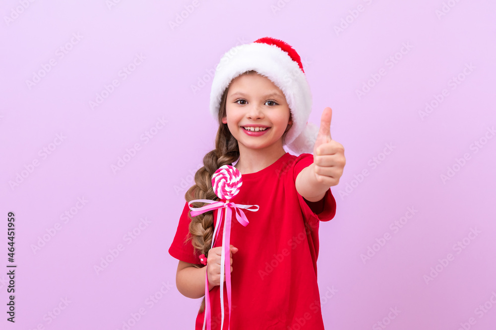 The child holds a Christmas candy on a stick in his hands and points his thumb up. The child holds a Christmas candy on a stick in his hands and points his thumb up.